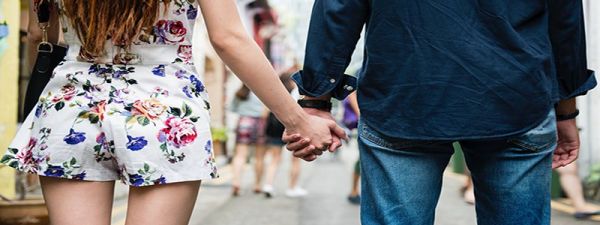 Male and female couple holding hands facing towards a busy street