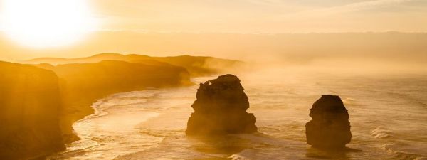 the twelve apostles at an orange sunset surrounded by mist on the water
